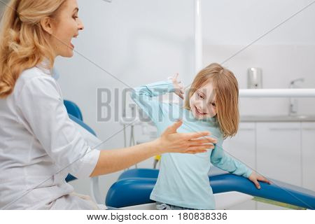Let us be friends now. Emotional cute prominent dentist giving a high five to her little patient after extracting her tooth