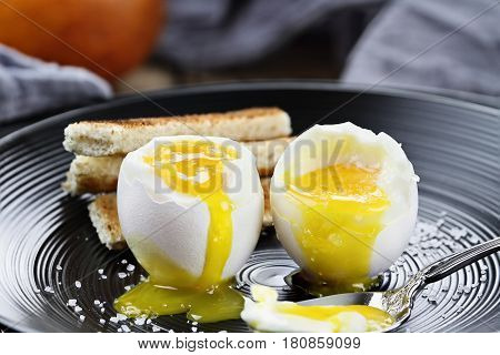 Two soft boiled eggs with toast soldiers and fruit in the background. Extreme shallow depth of field with selective focus.