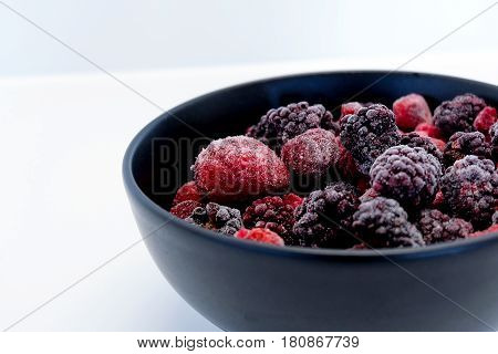 Frozen Berries in black bowl on white surface
