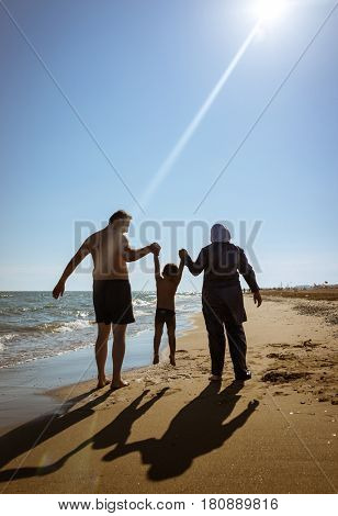 Muslim family, dad and mom with burkini on the beach walking near sea