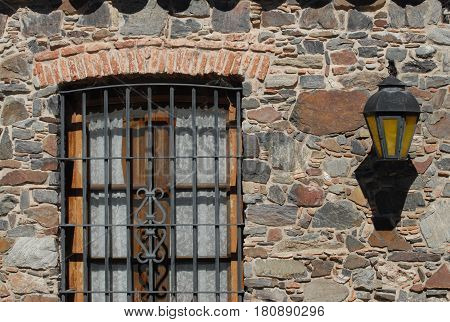 Detail of window with iron grate and iron lantern on stone wall