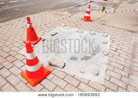 Plastic red cones warn pedestrians about repair of the sidewalk and sewerage hatchway. Moscow Russia.