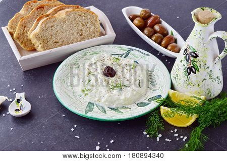 Greek traditional sauce tzatziki with olives, olive oil jar, lemon and bread on a grey abstract background. Healthy eating concept