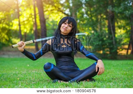 Young girl sitting on the grass and holding samurai sword. Original cosplay character