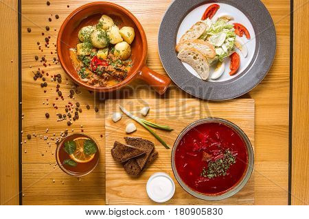 A set of dishes borsch with sour cream garlic onion potatoes in a pot and Caesar salad on a wooden table