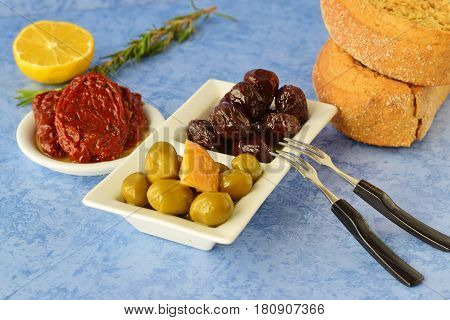 A set of dishes of greek cuisine: olives, sun dried tomatoes, lemon, beetroot, jar with olive oil and traditional dry bread. Traditional Greek food. Mediterranean lifestyle.