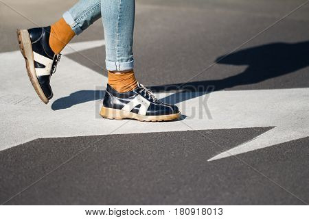 side view close up of a fashionable young woman legs wearing black shoes and blue jeans walking from left to right on the street natural daylight