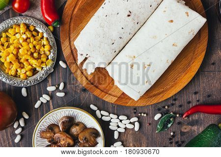Vegetarian Burrito On Wooden Board Over Black Table Surrounded By Ingredients.