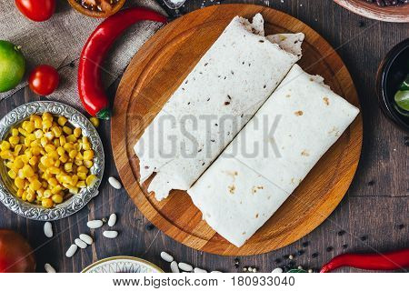 Vegetarian Burrito On Wooden Board Over Black Table Surrounded By Ingredients.