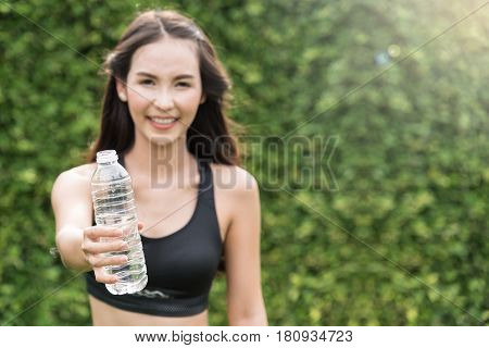 Asian woman in sportswear holding bottle of water on natural background. freshness happiness relaxing and smiling.