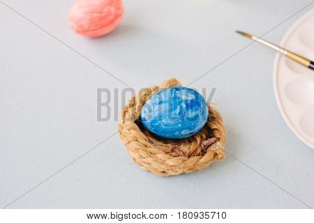 Deep Blue Easter Egg On Nest Over Bright Background.