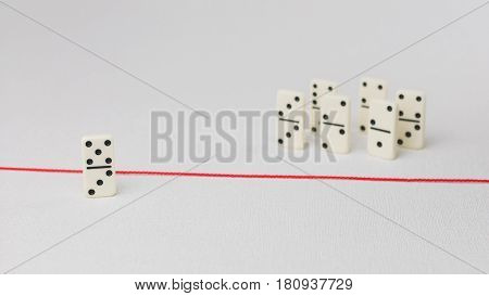 Expelled from the group, unable to cross the red line that separates them. Scene with group of domino. Concept of accusation guilty person, bulling or outcast in the team. Bright background.