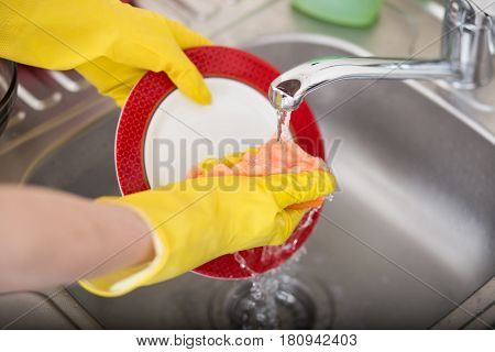 Cleaning dishware kitchen sink sponge washing dish. Close up of female hands in yellow protective rubber gloves washing