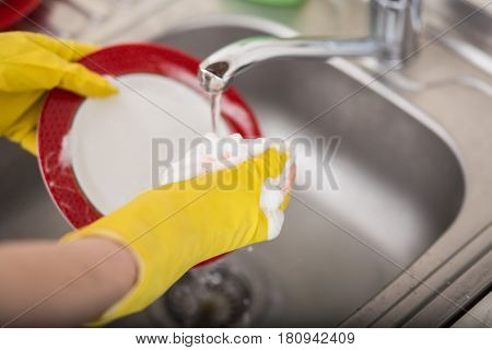 Cleaning dishware kitchen sink sponge washing dish. Close up of female hands in yellow protective rubber gloves washing