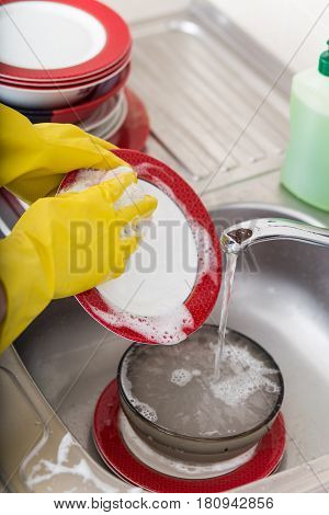 Cleaning dishware kitchen sink sponge washing dish. Close up of female hands in yellow protective rubber gloves washing