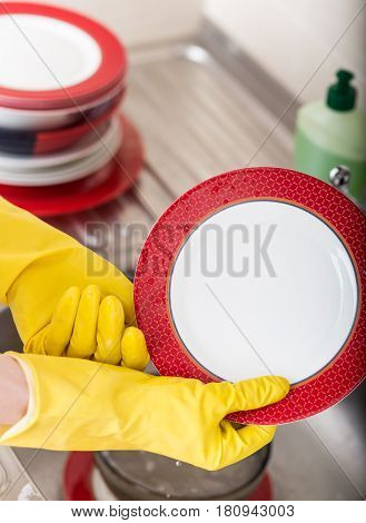 Cleaning dishware kitchen sink sponge washing dish. Close up of female hands in yellow protective rubber gloves washing