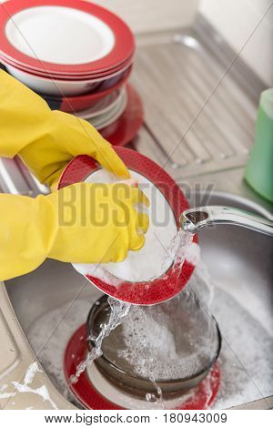 Cleaning dishware kitchen sink sponge washing dish. Close up of female hands in yellow protective rubber gloves washing