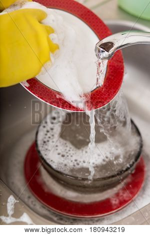 Cleaning dishware kitchen sink sponge washing dish. Close up of female hands in yellow protective rubber gloves washing