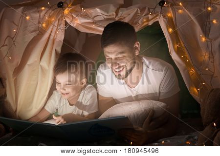 Father and son reading book in hovel at home
