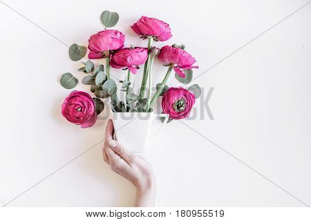 Modern spring design with bright pink flowers in hand on white desk background top view moke up