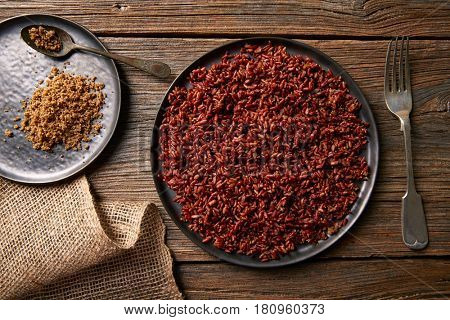 Red wild rice with sesame gomasio seasoning in a white plate over wooden board