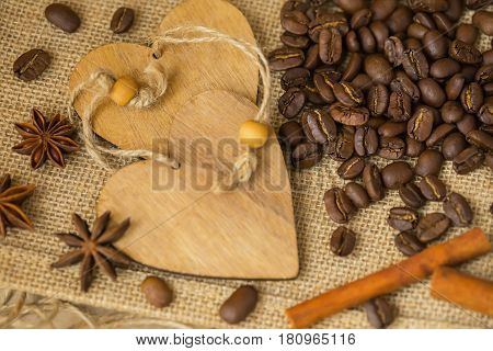 Grains of roasted coffee on sackcloth background with decorative wooden hearts. Coffee background for creative concepts for any day or advertising