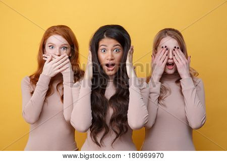Three women covering their ears, eyes and mouth over yellow background