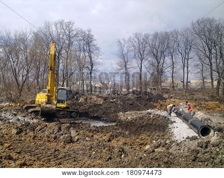 The workers cover the culvert with waterproofing. Nearby there is an excavator.