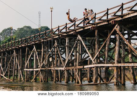 Kanchanaburi Thailand - December 09 2013: A child jumping from Saphan Mon (Mon Bridge) to Song Karia river with tourists taking photograph from the wooden bridge