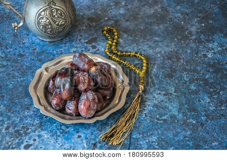 Dried Date Fruits Or Kurma Served On A Old Vintage Palte With Ornaments And Beads On A Blue Stone Ba