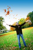 Young man having fun throwing up piles of autumn leaves .