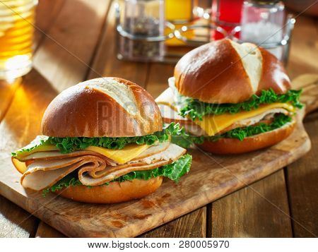 two cold cut style turkey and cheese sandwiches on pretzel buns
