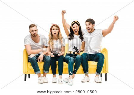 Emotional Young Friends Sitting On Sofa And Playing With Joysticks Isolated On White