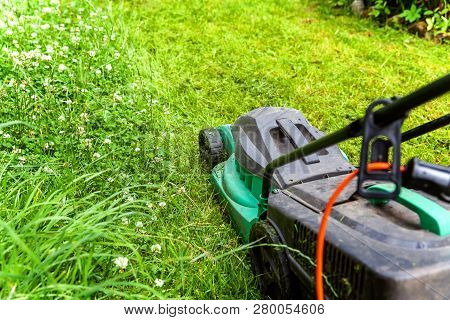Man Cutting Green Grass With Lawn Mower In Backyard. Gardening Country Lifestyle Background. Beautif