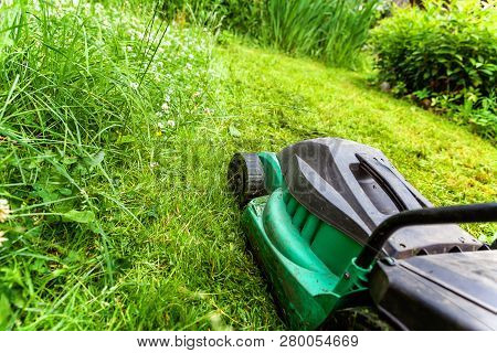 Man Cutting Green Grass With Lawn Mower In Backyard. Gardening Country Lifestyle Background. Beautif