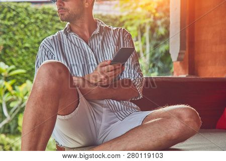 Man Using Smart Phone On A Terrace Sofa In Summertime.