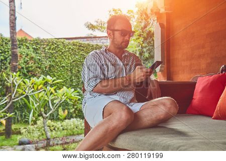 Man Using Smart Phone On A Terrace Sofa In Summertime.