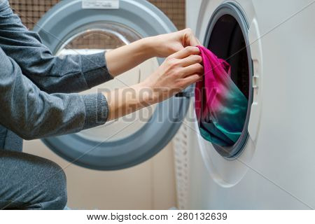 Photo of woman folding clothes into washing machine