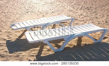 Two Sunlongers On The Sand Beach In Summer.