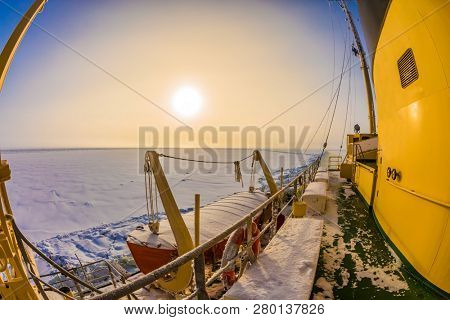 The strip of ice crumb spreads behind the icebreaker. The excursion to the arctic tourist cruise on the sea icebound. Dim polar sun in Lapland. The concept of active and extreme tourism