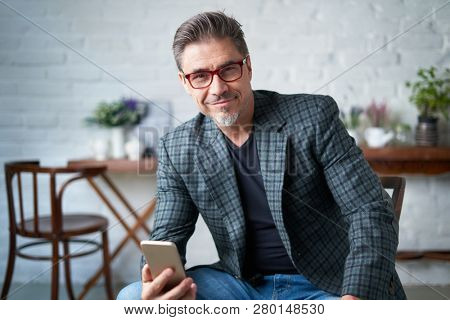 Portrait of happy older white man with gray hair wearing jacket smiling using smart phone. 
 .