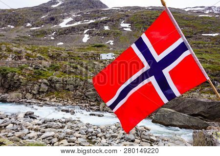 Norwegian Flag Waving On Wind And Camper Car In Mountains In The Background. Travel, Holidays And Ad
