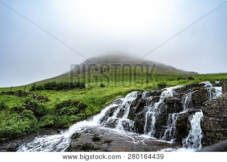 Beautiful And Peaceful Waterfall (long Exposure) With Green Grass And Small Houses In Foggy Weather 
