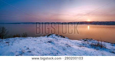 The Snow-covered Coast Of The River With The Winter Sun Setting Over The Horizon. Beautiful Sky With