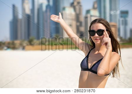 Young Woman In Bikini And Sunglasses Pointed On Skyscrapers While Relaxing On The Jbr Beach In Dubai