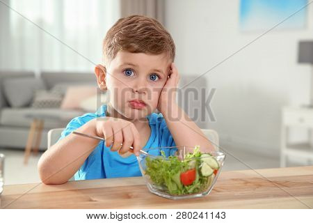 Emotional Little Boy Eating Vegetable Salad At Table In Room