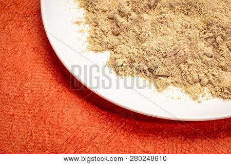 maca root powder on white ceramic plate against red textured paper