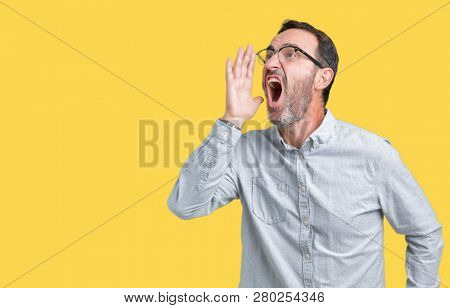 Handsome middle age elegant senior man wearing glasses over isolated background shouting and screaming loud to side with hand on mouth. Communication concept.