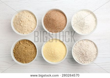 Bowls With Different Types Of Flour On White Wooden Background, Top View