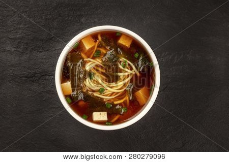 A Bowl Of Miso Shiru Soup With Tofu, Scallions, Noodles, And Wakame Seaweed, Shot From The Top On A 